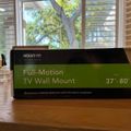 A TV wall mount product box on a wooden desk near a window with blinds