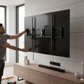 A man installing or adjusting a large flat-screen TV mounted on a wall bracket in a modern living room