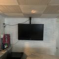 Interior room with wood-paneled ceiling and walls, featuring a wall-mounted flat screen TV, wicker furniture, and decorative items on a side table