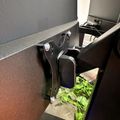 A mechanical device or machine with metal components and green leafy vegetables or plant material visible in the lower portion