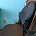 A brown upholstered chair with a black lumbar support cushion positioned against a light blue wall near an electrical outlet
