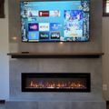 Modern living room with wall-mounted TV displaying streaming service menu above electric fireplace with marble surround