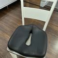 A black cushion with a cutout center placed on a white wooden chair in a room with dark hardwood flooring