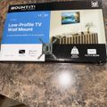 A product box for a Mount-It low-profile TV wall mount, displayed on a marble countertop. The box shows the model number MU-2033X, features a blue section with product details, and includes an image of a mounted TV on a white wall. The packaging indicates compatibility with 13 to 50 inch TVs and VESA standards.