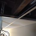 Interior view of an unfinished basement or ceiling area showing exposed wooden beams, white drywall panels, and electrical wiring or cables hanging down