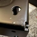 Close-up view of a metal mechanical part or component with circular holes and mounting hardware on a textured surface
