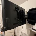 A large flat-screen TV mounted on an adjustable wall bracket in a white room with wooden flooring and white furniture