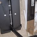 Black adjustable desk or table frame components laid out on carpet during assembly, with instruction manual and packaging materials nearby