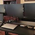 A desk setup with multiple computer monitors, laptops, and various electronic devices arranged on a dark surface in what appears to be a home or office environment.