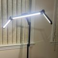 A modern adjustable LED desk lamp with articulating arms positioned near a window with vertical blinds
