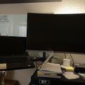A home office workspace with a laptop computer, large monitor, and desk area containing books, papers, and office supplies