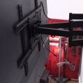 A black adjustable TV wall mount bracket installed on a white wall with red lighting visible in the background