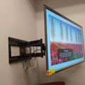 Wall-mounted TV on articulating bracket displaying a scenic image of red tulip fields with blue sky