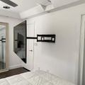 Modern bedroom with wall-mounted TV on articulating arm, mirrored closet doors, white walls, and exposed ceiling beams