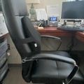 Black leather office chair at wooden desk with computer monitor and office supplies in professional workspace