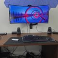 Computer workstation with curved ultrawide monitor displaying desktop wallpaper, wireless keyboard and mouse on desk pad, flanked by small speakers