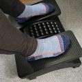 Person wearing colorful socks using a black ergonomic footrest with massage rollers under a desk