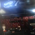 A living room entertainment setup with a large TV mounted on a decorative red patterned wall, with audio equipment and electronics on a dark shelf below