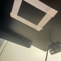 A rectangular opening cut in a ceiling with white tape around the edges, likely for installing a light fixture or ventilation fan