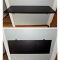 Two views of a black fold-down desk or table mounted between white walls in a narrow space with wooden flooring - shown open in top image and closed in bottom image
