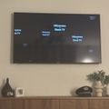 Wall-mounted Hisense Roku TV displaying the home screen interface, positioned above a wooden media console with decorative items