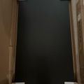 A large dark rectangular object, likely a TV or monitor, in cardboard packaging with white protective foam corners