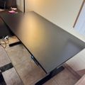 A black height-adjustable desk with electronic controls positioned on a tiled floor in a modern room setting
