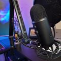 Gaming setup with microphone on boom arm, computer with blue LED fans, and monitor displaying colorful graphics in a room with purple ambient lighting