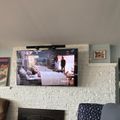 A flat screen TV mounted above a white brick fireplace displaying what appears to be a medical or hospital scene, with a white mantel shelf containing decorative items