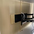 A black TV or monitor mounted on an articulating wall bracket attached to a beige wall panel, with cables visible