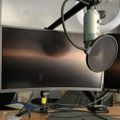A desktop computer setup with a curved monitor, keyboard, and a professional microphone with pop filter mounted on an adjustable arm above the workspace