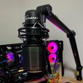 Professional microphone on adjustable boom arm positioned near gaming computer setup with RGB lighting