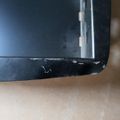 Close-up view of a damaged black electronic device corner showing cracks and wear on the edge