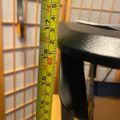A measuring tape showing measurements in inches is positioned vertically next to a black metal object, with a wire grid visible in the background