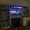 A living room with built-in white bookshelves surrounding a fireplace and mounted TV displaying a streaming service menu