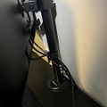 A black adjustable desk lamp or task light mounted on a stand, positioned against a white wall in what appears to be a corner or workspace area.