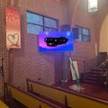 Interior of a church or chapel with brick walls, wooden pews, a large TV screen displaying content, and a banner with "faith hope LOVE" visible on the wall