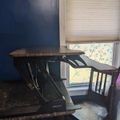 A standing desk converter placed on a kitchen counter next to a wooden chair, with a window and blue wall in the background