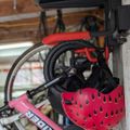 A pink bicycle with a red watermelon-patterned helmet hanging from the handlebars, stored in what appears to be a garage or storage area