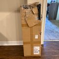 A large cardboard box leaning against a wall in a home interior, with packing materials and a shipping label visible on its surface.