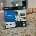 A Mount It low-profile tilt TV wall mount package box displayed on a granite countertop in a modern kitchen, with a home interior visible in the background.