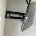 Wall-mounted TV bracket installed on white wall with cables visible and TV partially shown