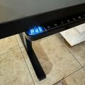 A black electronic device or appliance with a blue digital display showing "Hot" sits on a tiled floor next to some papers