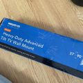 A blue product box for a Mount-It Heavy-Duty Advanced Tilt TV Wall Mount for 37-90 inch TVs lying on a wooden floor