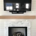 Wall-mounted TV above marble fireplace with wood mantel on white shiplap wall