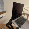 A laptop computer mounted on an adjustable black stand positioned on a white desk in an office or workspace setting