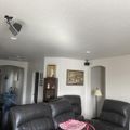 Modern living room with dark leather furniture, track lighting, white walls, and artwork including a Japanese wave print