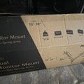 Cardboard box for a dual monitor mount with gas spring arms that fits 13-32 inch monitors, showing product specifications and diagrams on the packaging