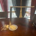 A white desk lamp with yellow cord sits on a dark wooden table near a window with blinds and red curtains