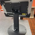 A tablet mounted on a black adjustable stand with a circular base, positioned on a counter in what appears to be a restaurant or commercial setting